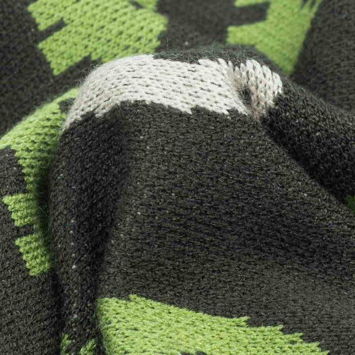 Close-up of a knitted textile with a dinosaur pattern in green, and off-white, showing the knit texture and color blocking