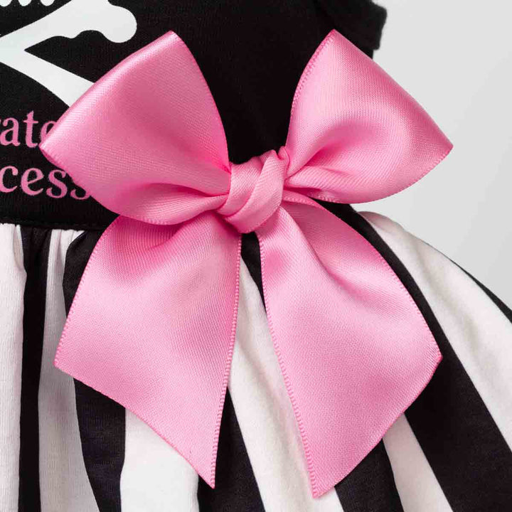 Close-up of a pink satin bow tied around a black and white striped skirt, with part of a black top showing white text