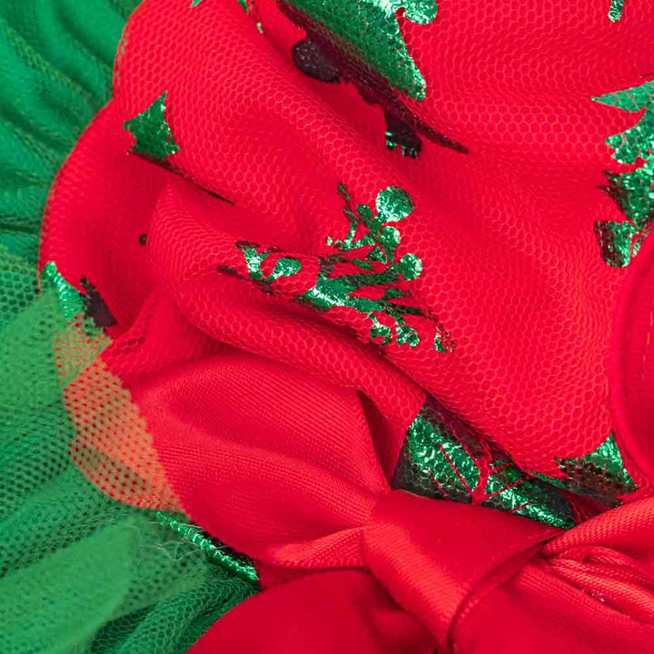 Close-up of red Christmas dog dress fabric with green tree print, layered tulle, and satin bow.