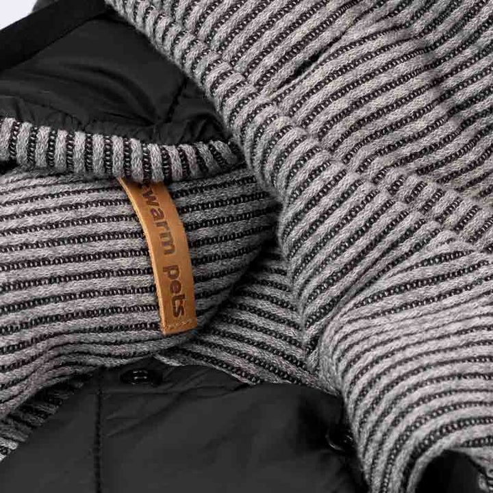 Close-up fabric detail of dog coat showing gray striped knit with Fitwarm label and quilted lining.