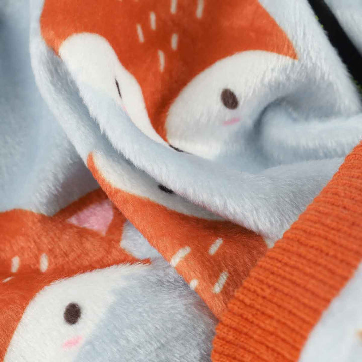 Close-up of light blue fleece dog pajamas with all-over cartoon fox print and orange trim, showcasing plush material.