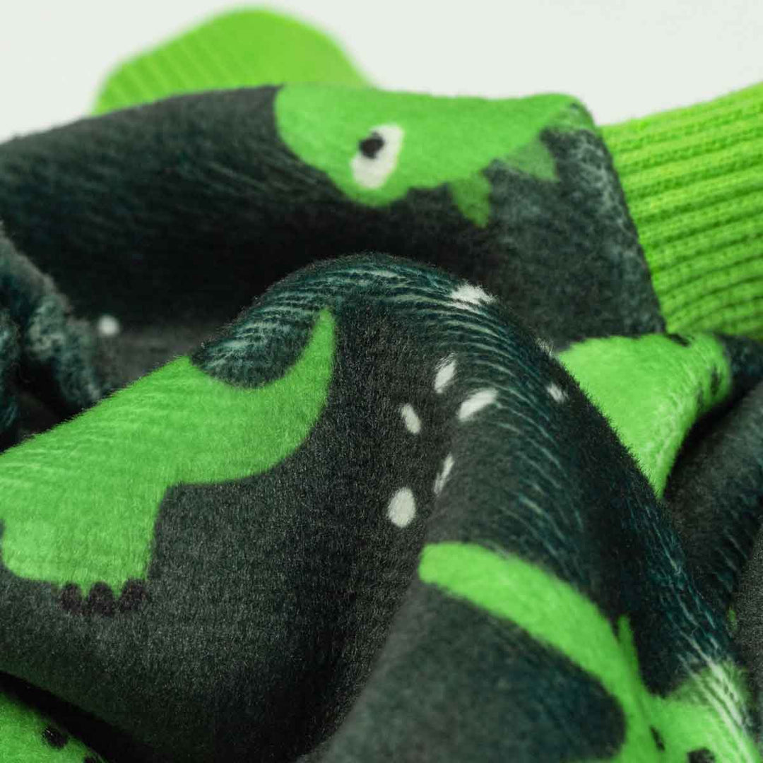 Close-up of soft gray dog pajamas with a repeating green dinosaur print and green ribbed cuffs.