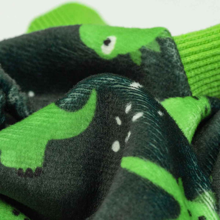 Close-up of soft gray dog pajamas with a repeating green dinosaur print and green ribbed cuffs.