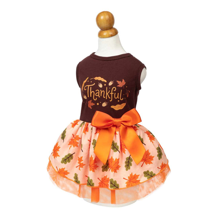 Sleeveless dog Thanksgiving dress displayed on a mannequin with a light peach tulle skirt with an orange and green leaf print, featuring a large orange satin bow at the waist