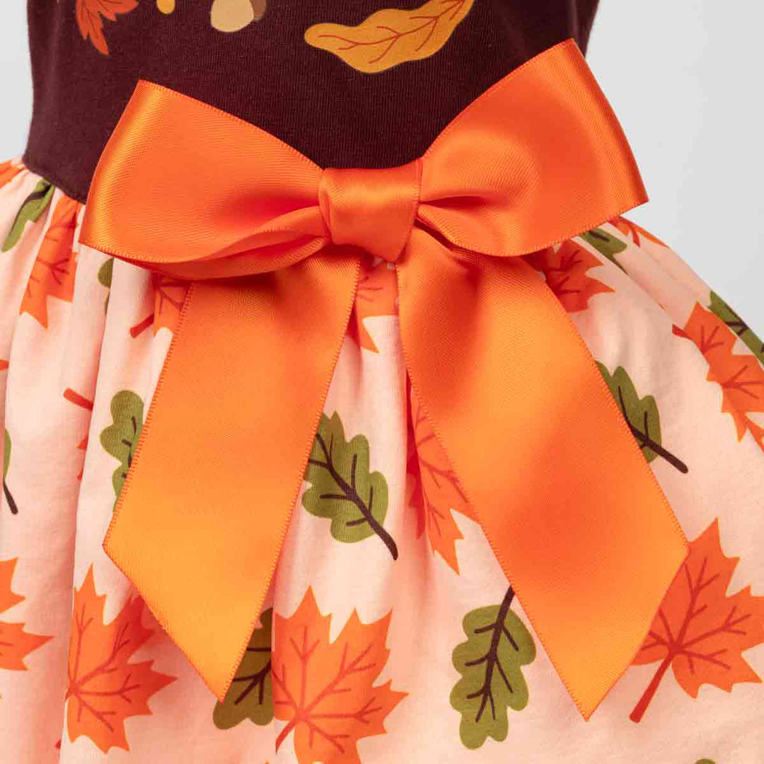 Close-up of a dog tulle dress featuring a large orange satin bow at the waist, with a peach skirt printed with orange and green autumn leaves