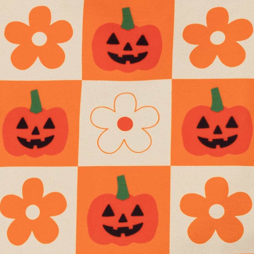 Fabric pattern featuring orange and cream squares, with four orange flower motifs and four orange jack-o'-lantern faces, including one cream flower in the center
