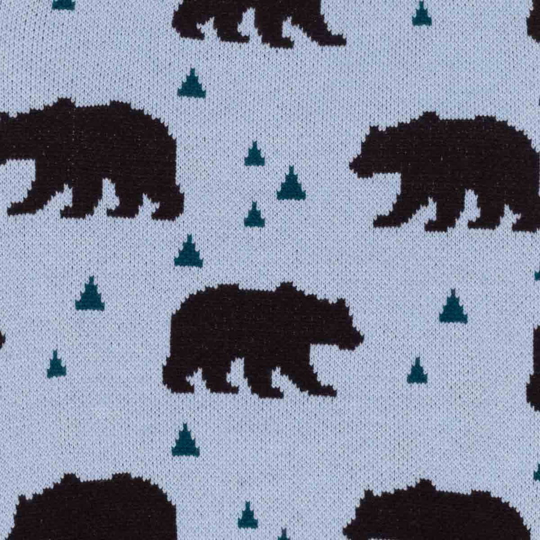 Close-up of knit fabric with a repeating pattern of dark brown bear and small teal tree on a blue background