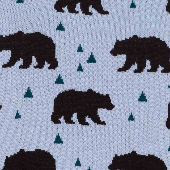 Close-up of knit fabric with a repeating pattern of dark brown bear and small teal tree on a blue background