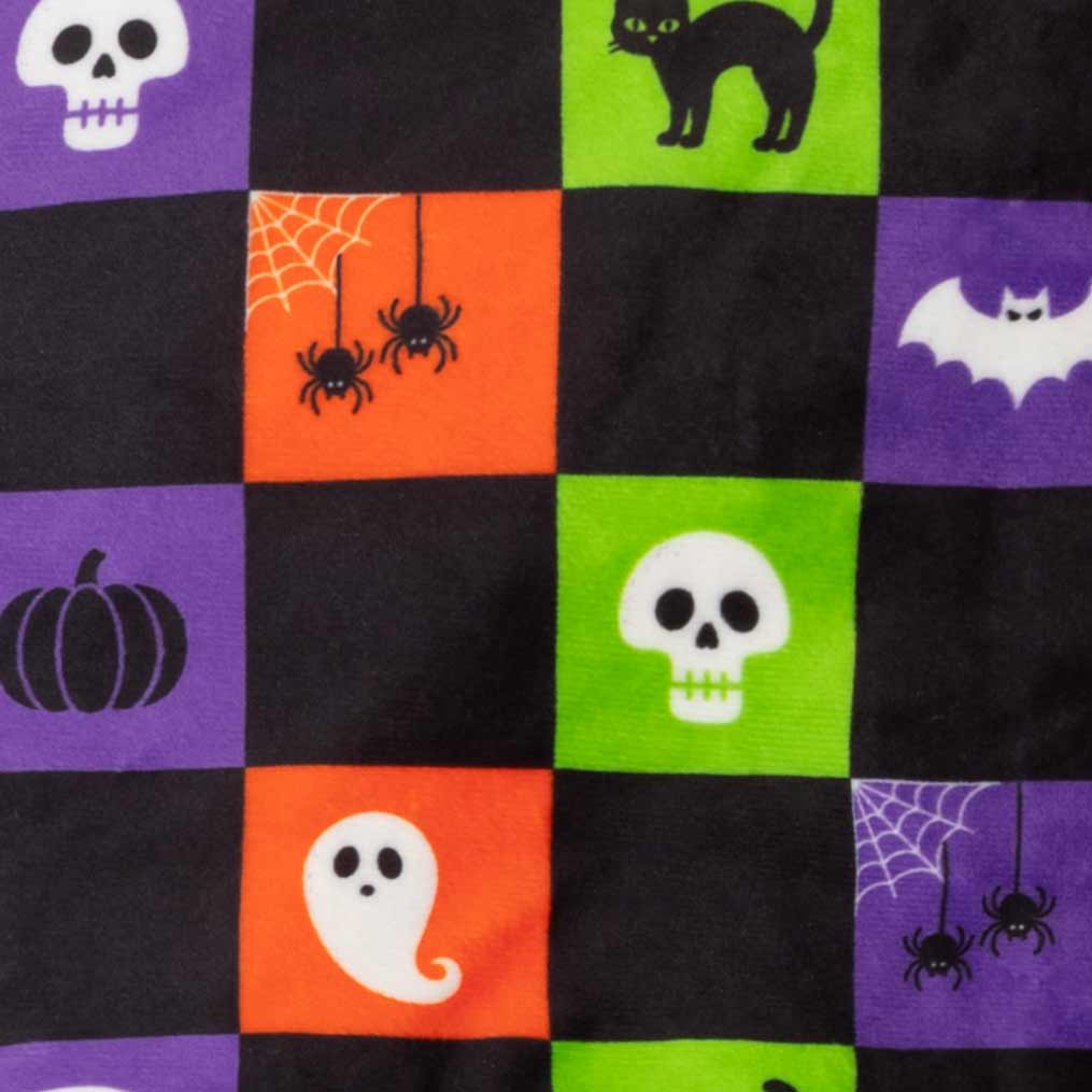 Close-up of a Halloween-themed checkered fabric featuring purple, black, orange, and green squares with printed motifs including skulls, a cat, bats, pumpkins, ghosts, spiders, and webs