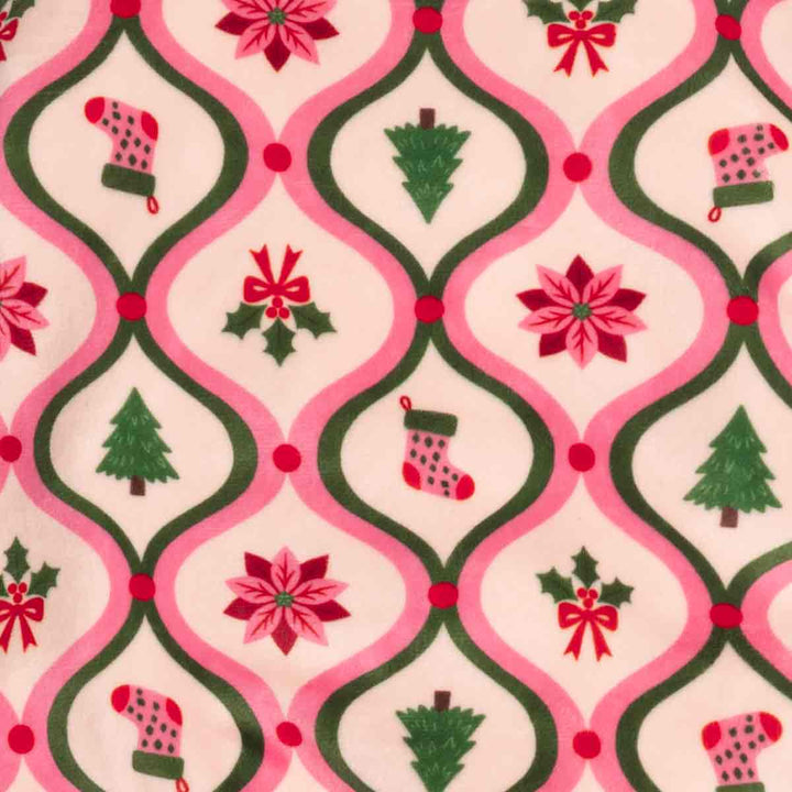 Close-up of a fabric on dog festive pajamas featuring a pink and green trellis design with Christmas prints including stockings, trees, holly, and poinsettias on a cream background