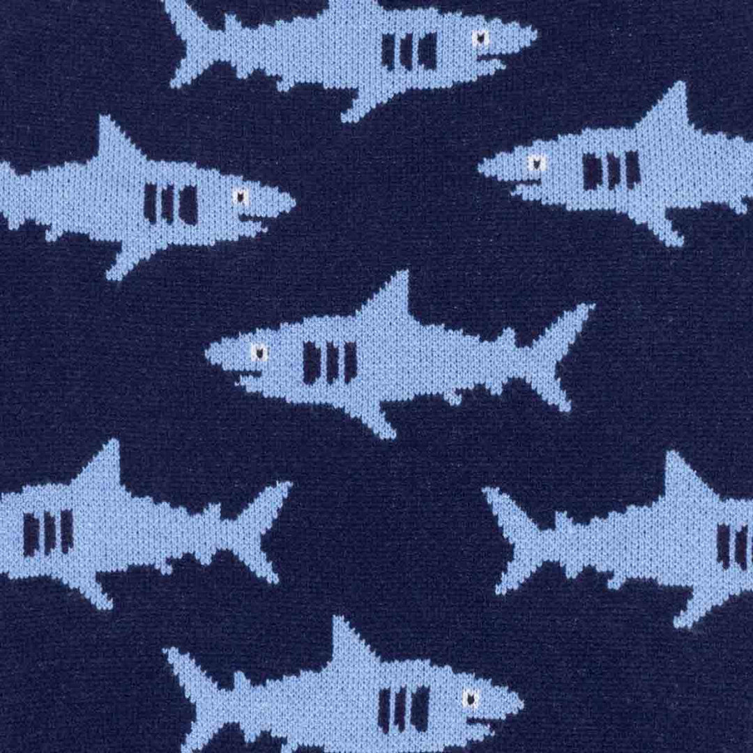 Close-up of a knitted fabric of dog winter sweater featuring a repeating pattern of light blue sharks on a dark navy blue background