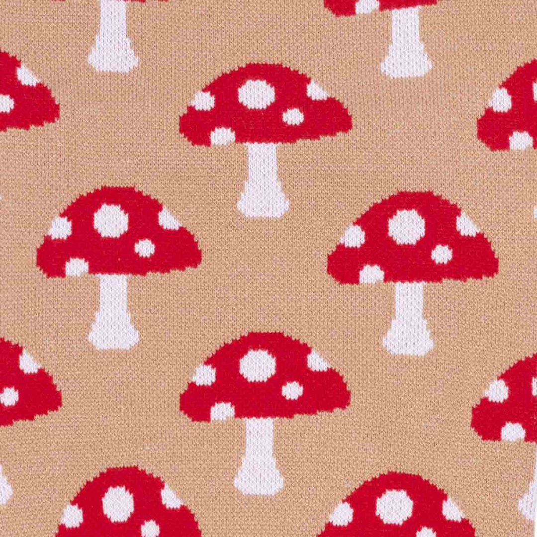Close-up of a knitted fabric with a repeating pattern of red mushrooms with white spots on a tan background