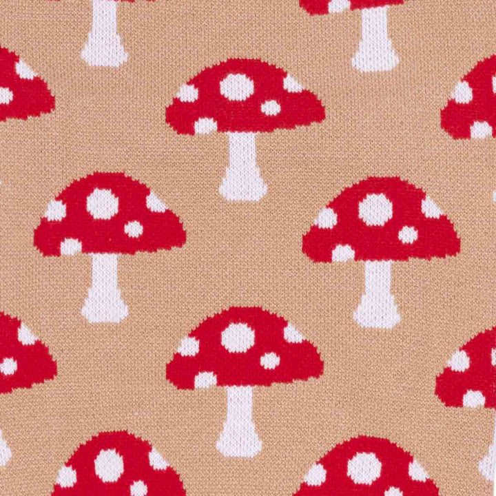 Close-up of a knitted fabric with a repeating pattern of red mushrooms with white spots on a tan background