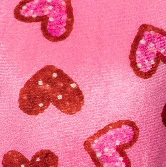 Close-up of pink dog dress with brown and pink heart prints on a soft velvet texture.