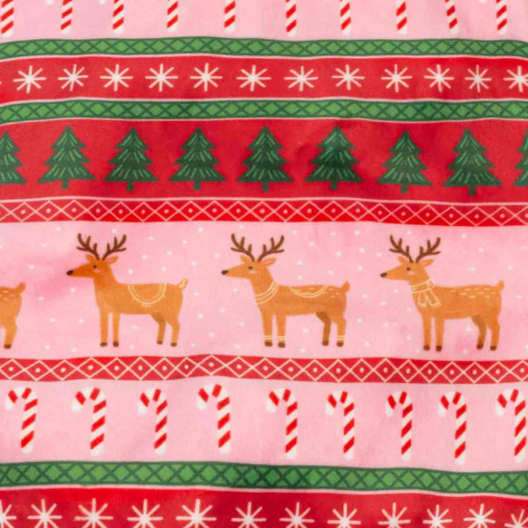 Close-up of a festive holiday fabric pattern featuring red and pink horizontal bands with white snowflakes, green pine trees, brown reindeer, candy canes, and green and red geometric borders