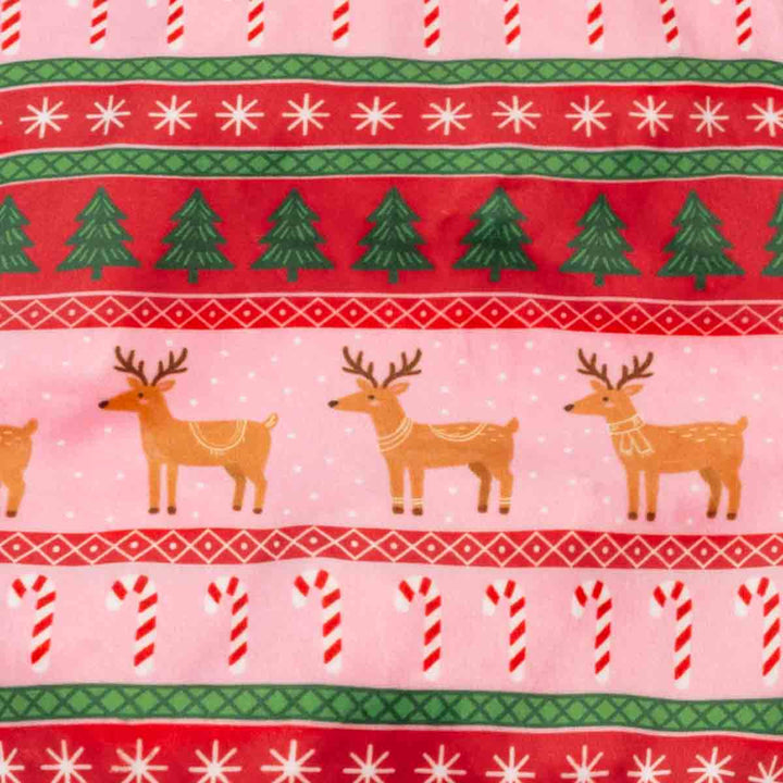 Close-up of a festive holiday fabric pattern featuring red and pink horizontal bands with white snowflakes, green pine trees, brown reindeer, candy canes, and green and red geometric borders