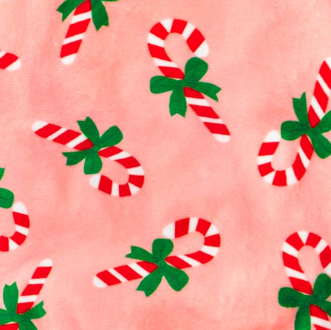Pink fabric pattern of dog pajamas featuring festive candy canes with green bows.