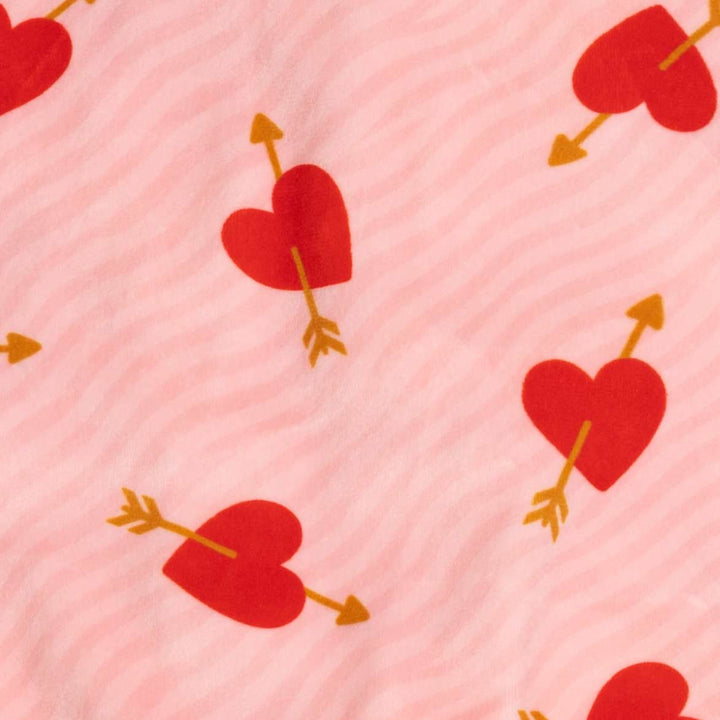 Close-up of a pink fabric with a repeating pattern of red hearts pierced by gold arrows