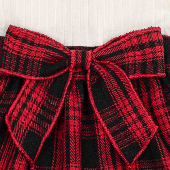 Close-up of a red and black plaid fabric bow with matching plaid trim, set against a light off-white textured background