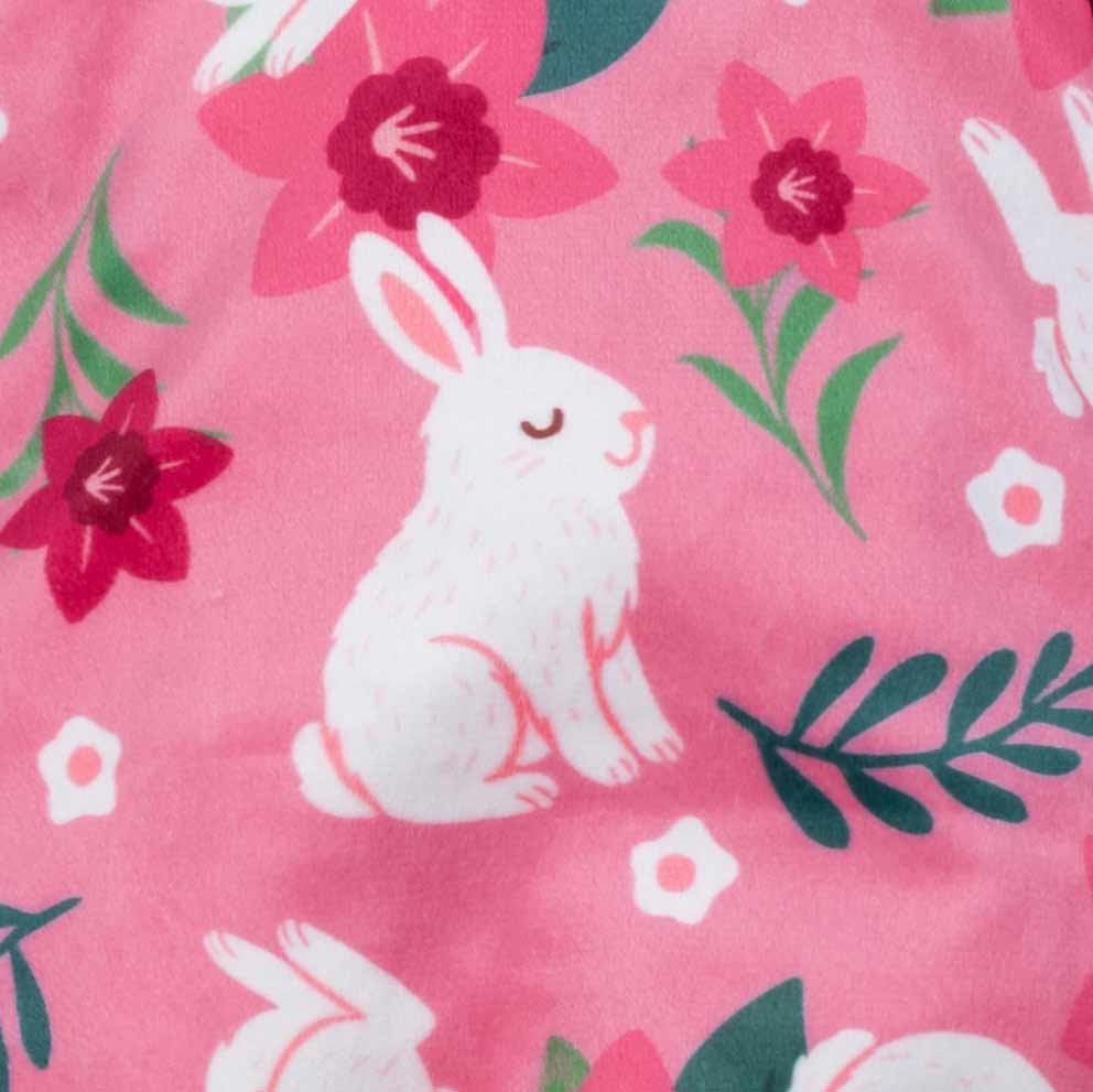 Pattern detail of pink bunny-themed dog pajamas featuring white rabbits and vibrant flowers.
