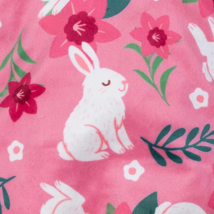 Pattern detail of pink bunny-themed dog pajamas featuring white rabbits and vibrant flowers.