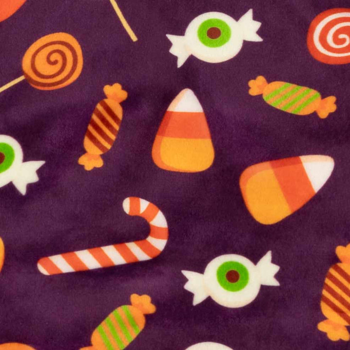 Soft purple Halloween dog pajama fabric with a playful pattern of candy corn, spiral lollipops, and eyeball treats.