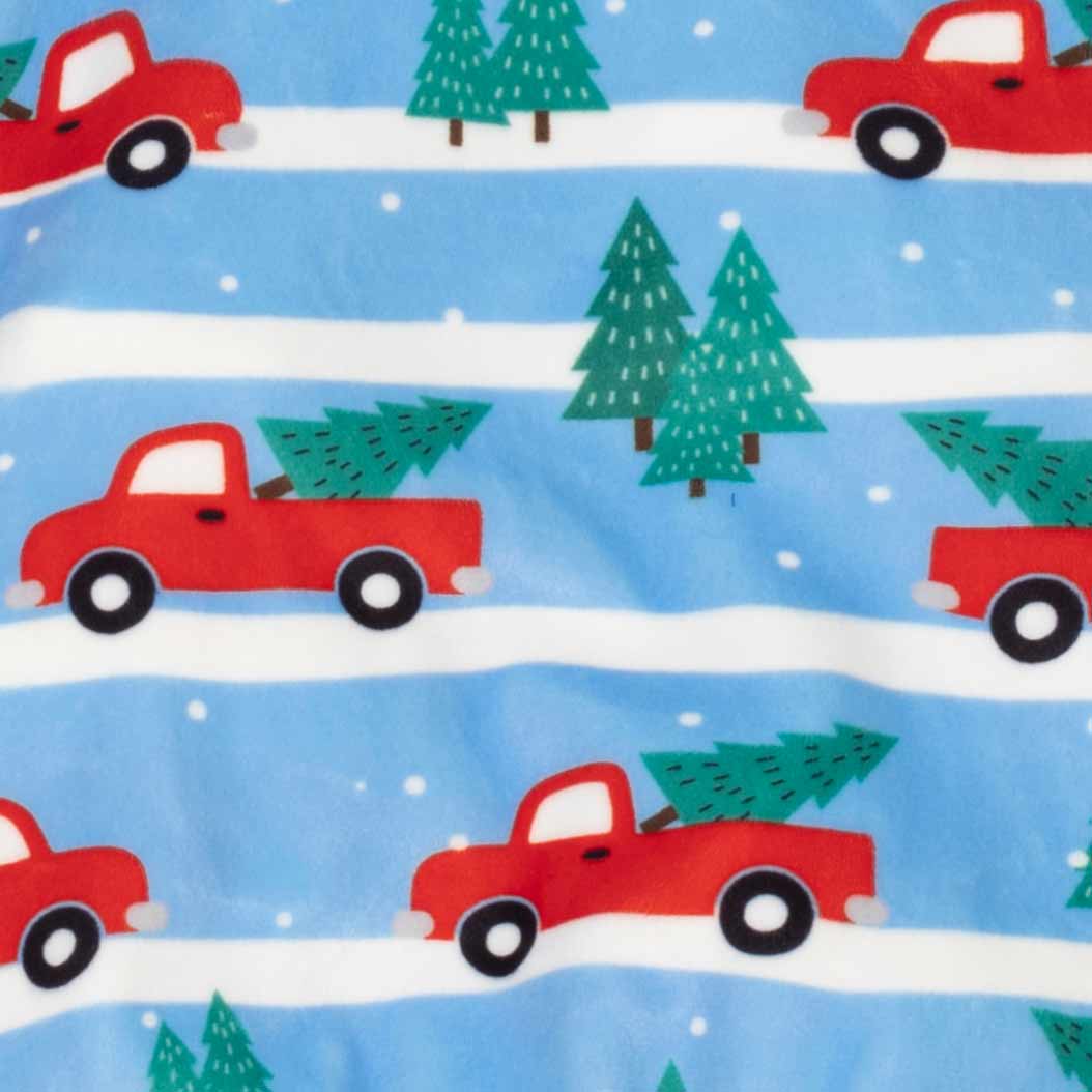 Close-up of a fabric pattern featuring red pickup trucks carrying green Christmas trees on a light blue background with white horizontal stripes and snowflakes