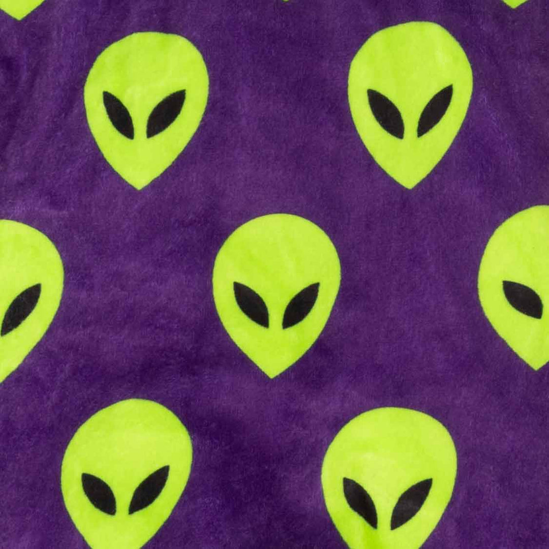 Close-up of a purple fabric with a repeating pattern of bright lime green alien heads with black eyes