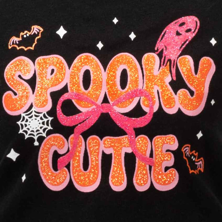 Close-up of a black garment featuring a glittery orange 'SPOOKY CUTIE' graphic with pink glitter accents, a pink ghost, white spiderwebs, and orange bats