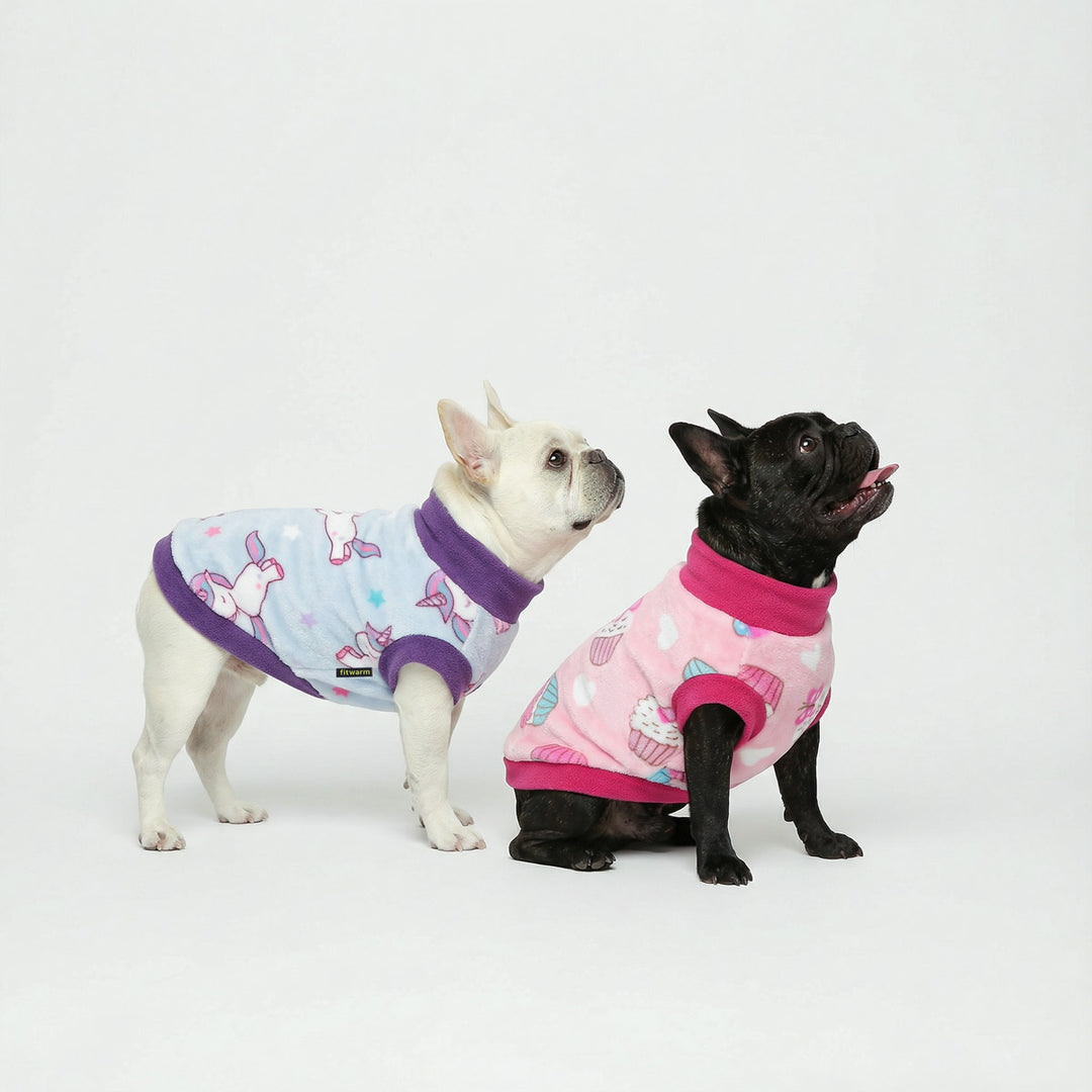 Two French bulldogs posing indoors in pastel dog fleece sweater designs with playful unicorn and cupcake prints