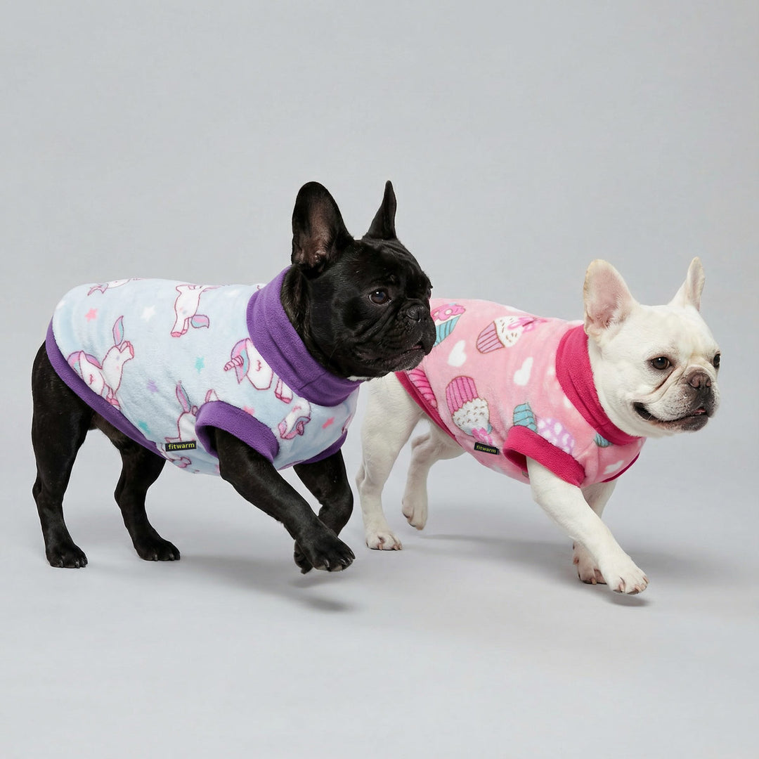 Two French bulldogs walking side by side wearing pastel fleece dog sweaters styles with playful prints
